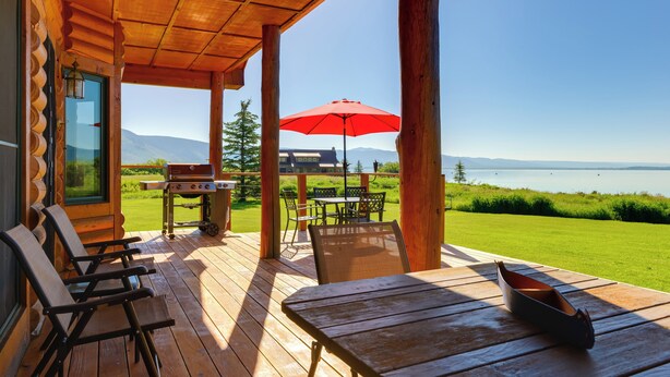 Een houten terras met buitenmeubilair, een barbecue en een rode parasol.