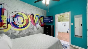 A bedroom with a bed, a TV, and a wall with colorful graffiti.