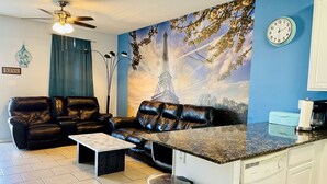 Ett vardagsrum med en svart lädersoffa, ett soffbord och en köksdel med en bänkskiva och köksutrustning.