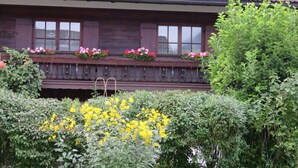 A wooden house with a balcony, surrounded by greenery and flowers. - Vacation apartment for 2 - 5 persons, approx. 85 m², living/sleeping room, 2 bedrooms, kitchenette, 2 bathrooms, 2 balconies, terrace (Bischofswiesen)