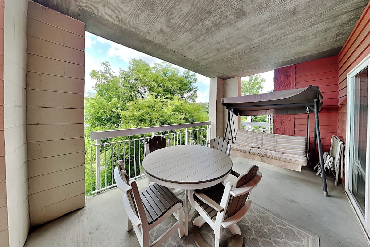 A covered patio with a round table and chairs, a swing, and a view of trees.