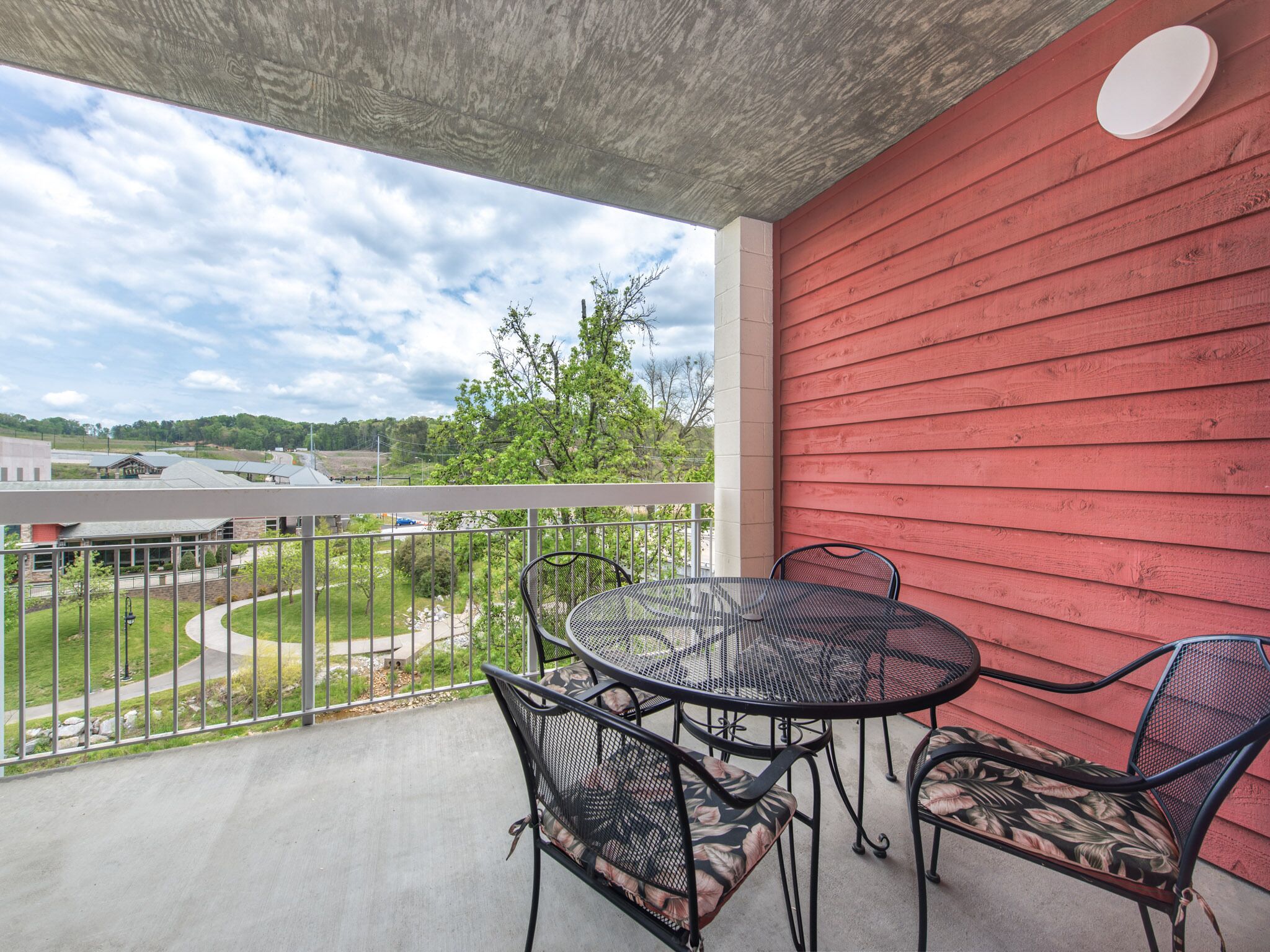 A balcony with a red wall, a round metal table, and two chairs with floral cushions.