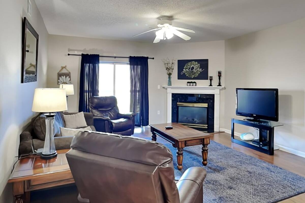 A living room with a leather sofa, a coffee table, a TV, a fireplace, and a ceiling fan.