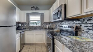 A kitchen with white cabinets, a granite countertop, a stainless steel refrigerator, a microwave, and a tiled backsplash. - Bear Crossing by Jackson Mountain Rentals (Pigeon Forge)