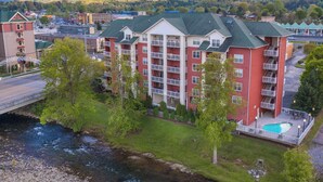 A multi-story hotel with a swimming pool, located near a river and surrounded by greenery and mountains. - Bear Crossing by Jackson Mountain Rentals (Pigeon Forge)