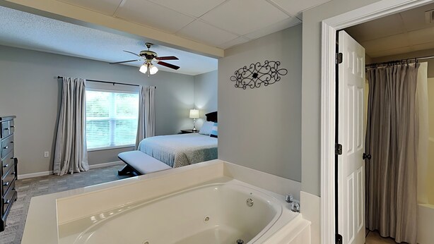 A bedroom with a large bathtub, a ceiling fan, a window with curtains, a bedside table, and a bed. - Bear Crossing by Jackson Mountain Rentals (Pigeon Forge)