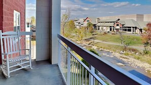 A balcony with a white rocking chair, a view of a river, and a row of houses in the background. - Bear Crossing by Jackson Mountain Rentals (Pigeon Forge)