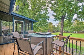 Une terrasse extérieure couverte, dotée d'un jacuzzi à débordement en verre, de fauteuils en osier et offrant une vue sur une pelouse bien entretenue et des arbres.