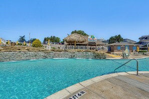Une piscine dotée d’une structure de toit en chaume, d’un mur en pierre et d’une enseigne indiquant « Tiki Bar ».