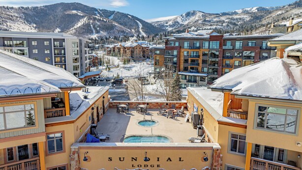 Vista de Sundial Lodge con un área de piscina, varios edificios y una montaña nevada al fondo.