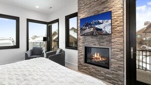 A modern bedroom with a large bed, a fireplace, and a TV mounted on the wall.