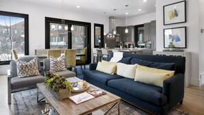 A modern living room with a dark blue sofa, a wooden coffee table, and a large window.