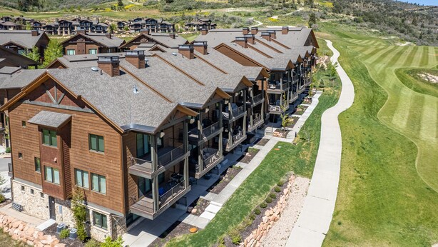 A row of modern, multi-story buildings with balconies, situated next to a well-maintained golf course.
