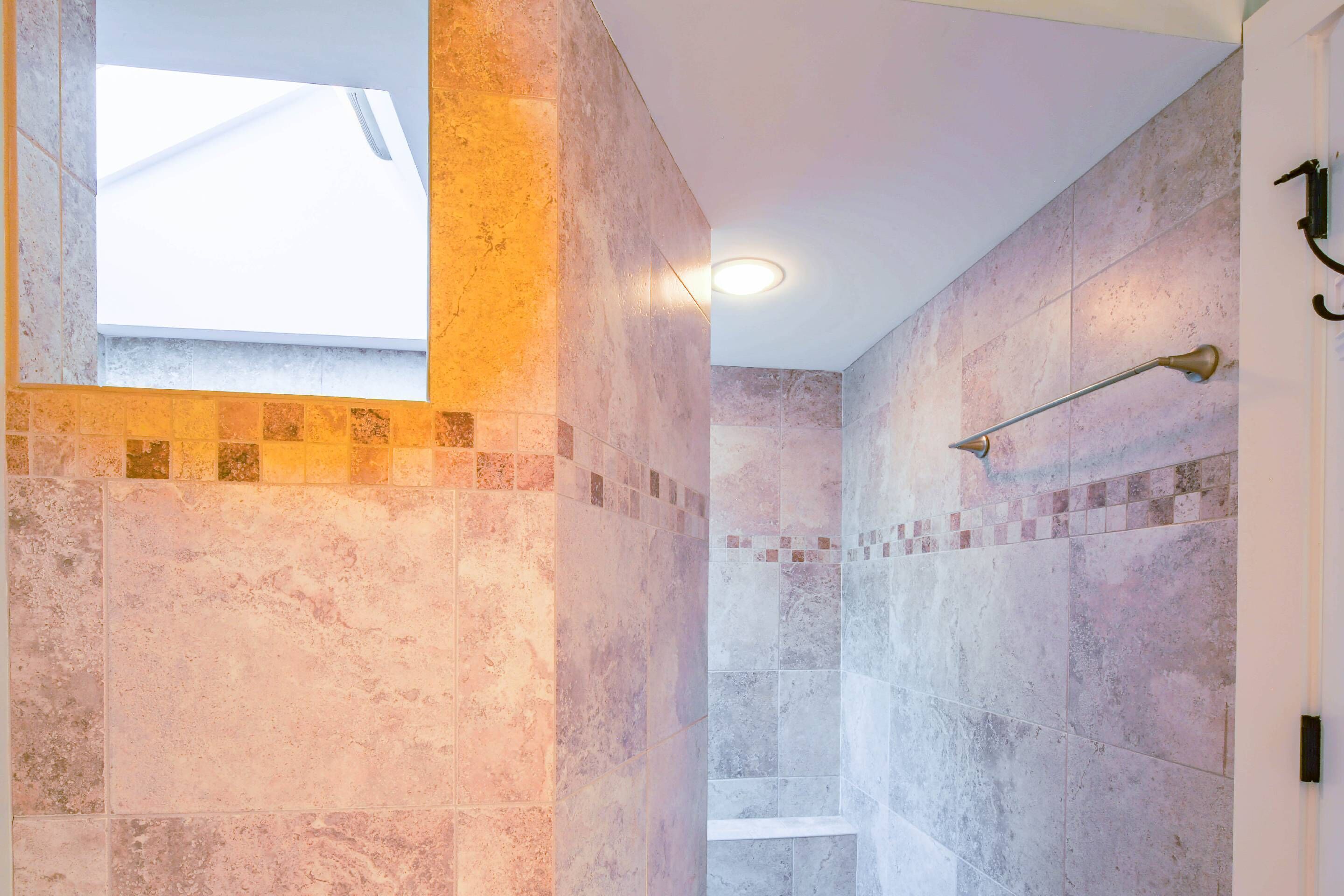 A modern bathroom with a skylight, a shower area, and a tiled wall with a mosaic border.
