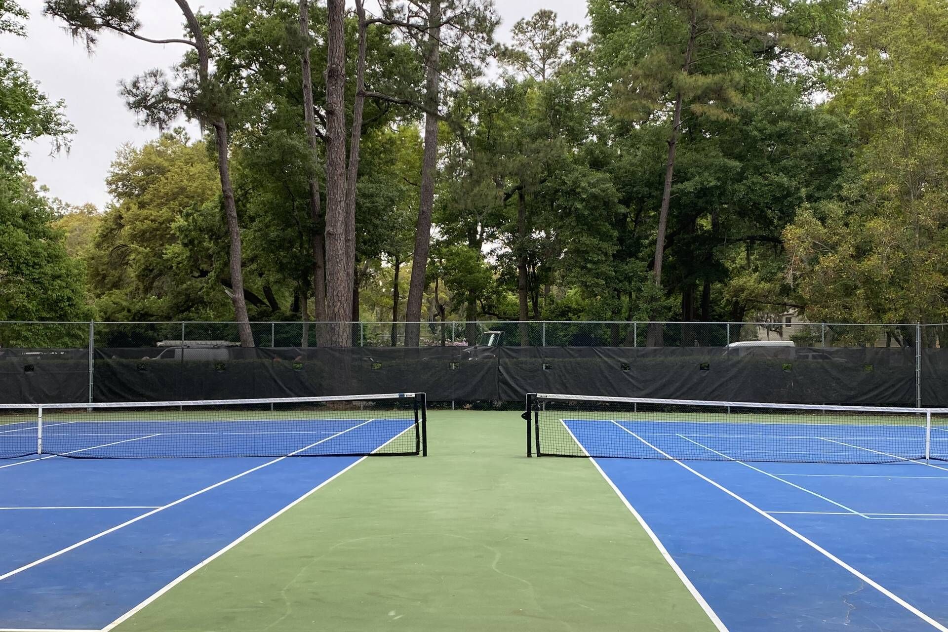 Un court de tennis en plein air, avec un filet au centre, entouré d’arbres.