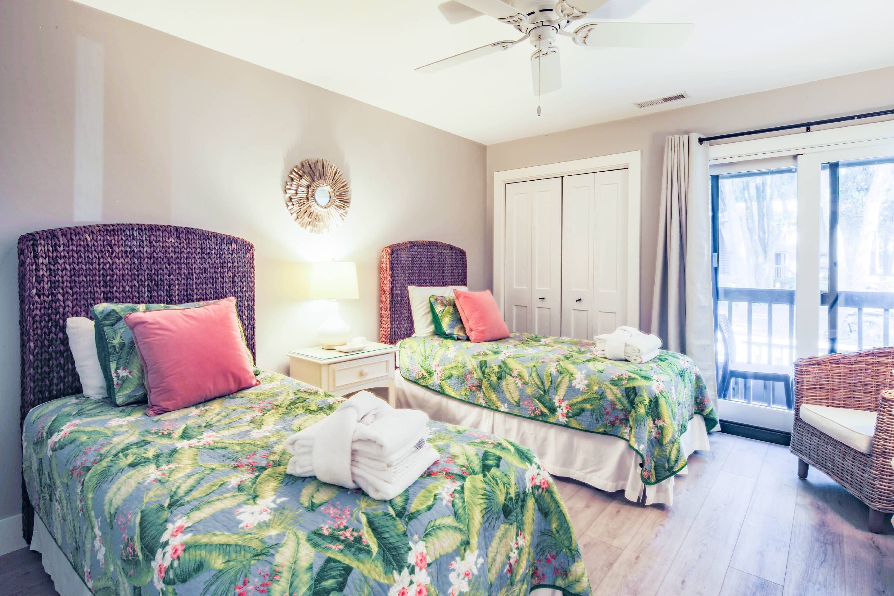 A hotel room with two beds, a ceiling fan, a large window with a view, and a wicker chair.