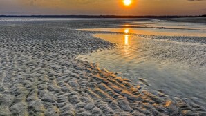 Una platja amb empremtes que condueixen a l'aigua, un atardeciment al fons i una mar tranquil·la.