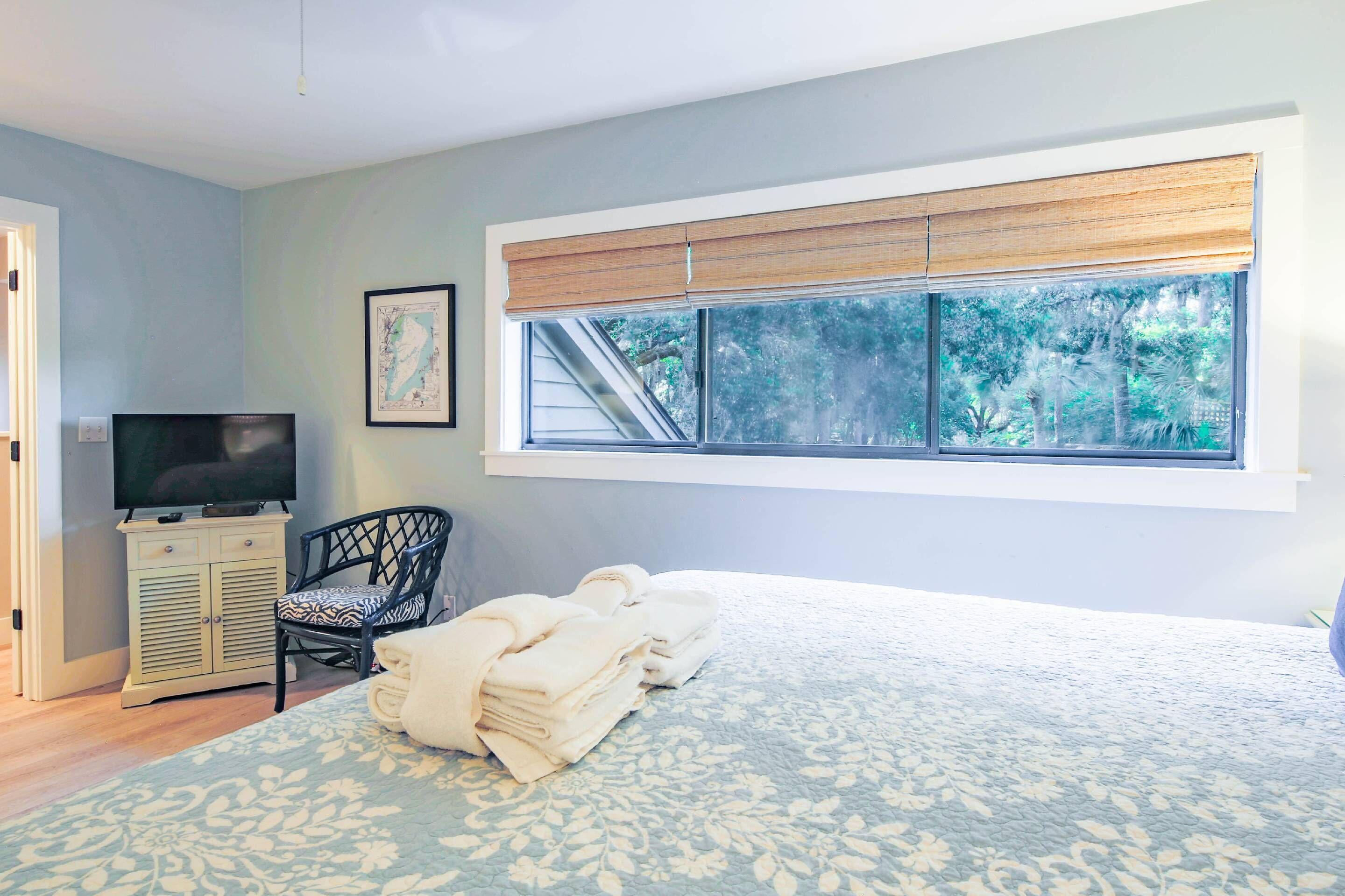 A bedroom with a bed, a television, a chair, and a window with a view of trees.