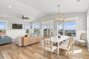 A spacious living room with a dining area, large windows, and a ceiling fan.