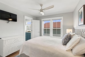 A bedroom with a bed, a ceiling fan, a window, and a door leading to a bathroom.