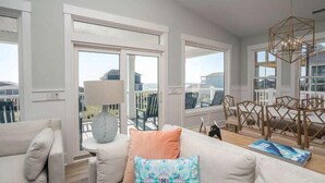 A modern living room with a sofa, a coffee table, and a dining area with chairs. - Beautiful Large 5 BR, 4.5 Beach Oasis Close, amazing ocean views and a private pool!  The Seaquel (Oak Island)