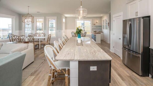 A modern kitchen with a central island, stainless steel appliances, and a dining area with wicker chairs. - Beautiful Large 5 BR, 4.5 Beach Oasis Close, amazing ocean views and a private pool!  The Seaquel (Oak Island)