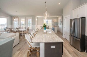 Een moderne keuken met een centraal eiland, roestvrijstalen apparatuur en een eethoek met rieten stoelen.