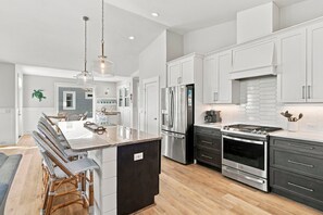 A modern kitchen with a central island, stainless steel appliances, and a dining area with wicker chairs.