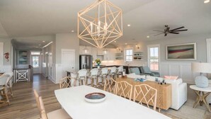 A spacious living area with a dining table, chairs, and a geometric ceiling light fixture. - Beautiful Large 5 BR, 4.5 Beach Oasis Close, amazing ocean views and a private pool!  The Seaquel (Oak Island)
