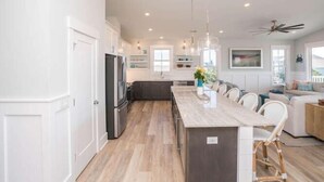 A modern kitchen with a central island, dark cabinetry, and a light wood floor. - Beautiful Large 5 BR, 4.5 Beach Oasis Close, amazing ocean views and a private pool!  The Seaquel (Oak Island)
