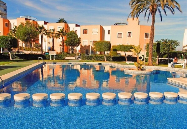 A swimming pool with a tiled deck, surrounded by buildings with balconies and palm trees.