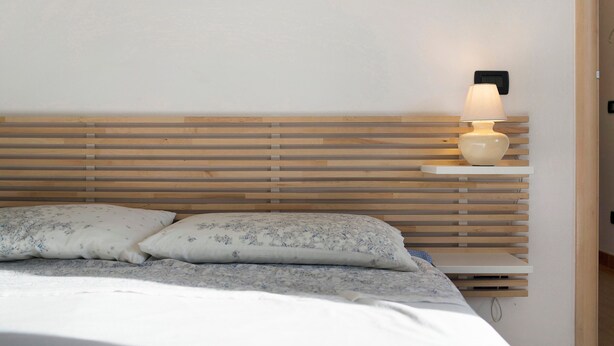 Uma cama com ripas de madeira, uma luminária de cabeceira e duas almofadas.
