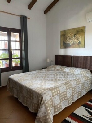Ein Schlafzimmer mit Bett, einem Vorhangfenster, einem Wandbild und einer Tür.
