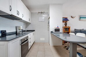 Une cuisine compacte avec des meubles blancs, un four à micro-ondes, une machine à café et une petite table à manger.