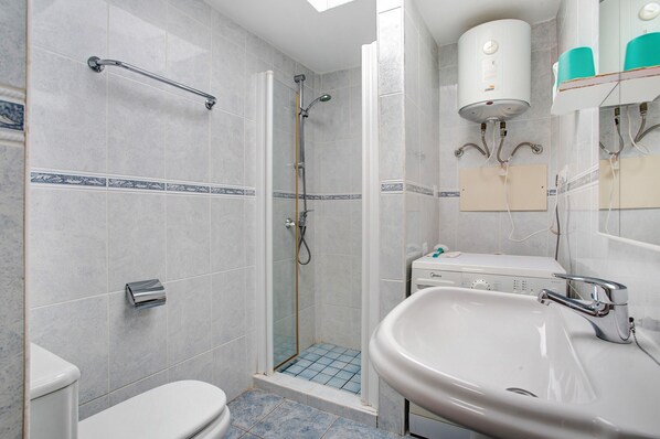 A bathroom with a shower, toilet, sink, and a water heater.