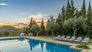 A swimming pool with lounge chairs and tables, surrounded by trees and a view of hills. - Historic Finca in Mallorca with Swimming Pool. 12 Guests  (Andratx)