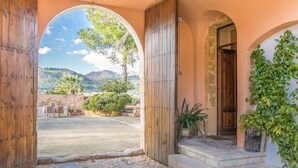 Un arc d'entrada dona pas a un pati amb vistes a un paisatge montanyós, paviment de pedra i plantes en testos.