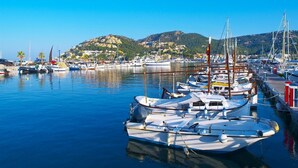 Un port esportiu amb embarcacions amarrades, aigua tranquil·la i un paisatge amb turons i edificis.
