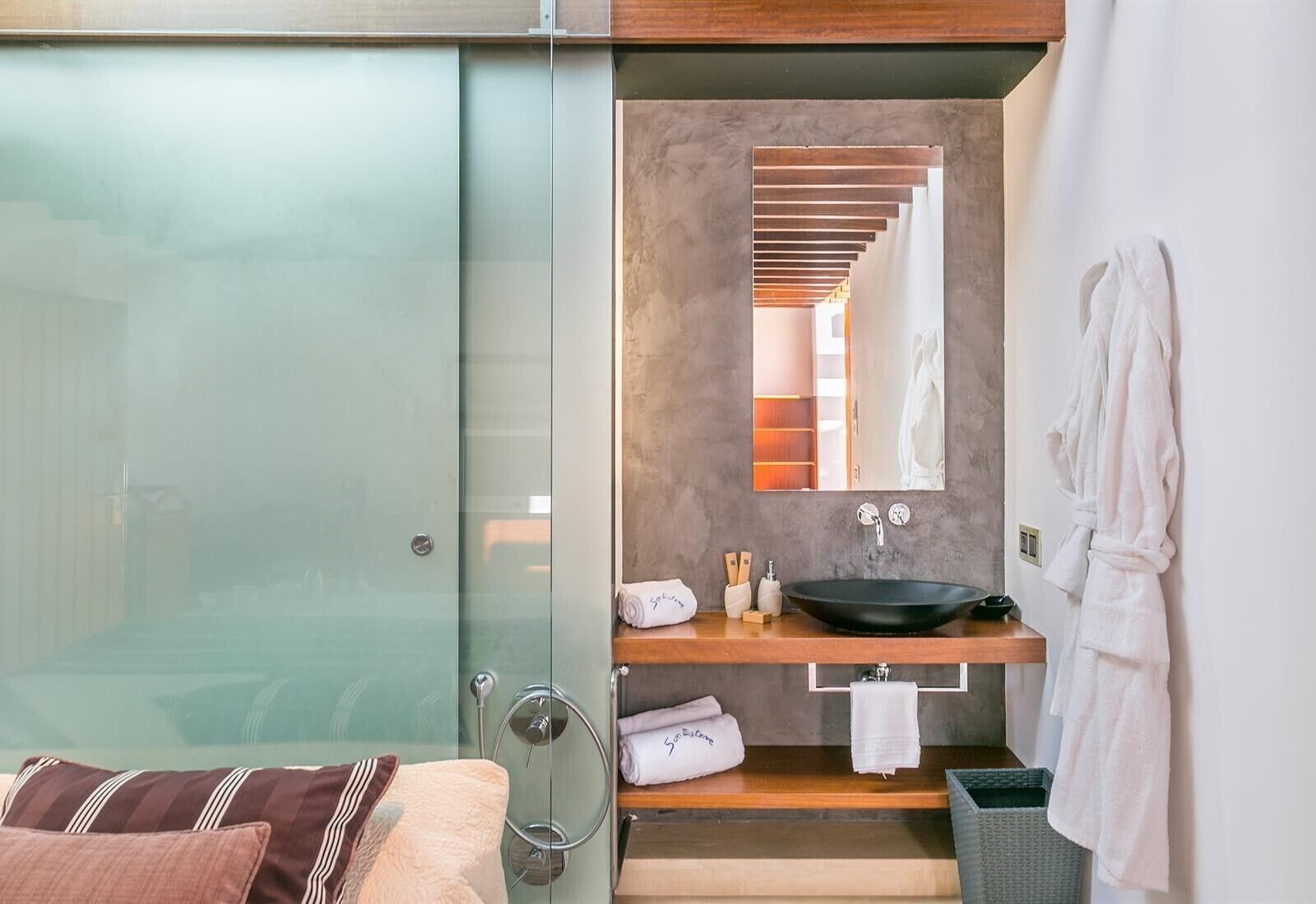 A modern bathroom with a glass shower enclosure, a wooden vanity, a large mirror, and a robe hanging on the wall.