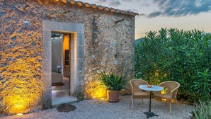 A stone building with a doorway, a small outdoor seating area with two chairs and a table, and a potted plant. - Historic Finca in Mallorca with Swimming Pool. 12 Guests  (Andratx)