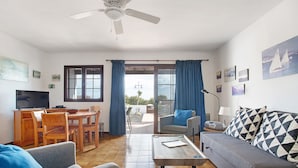 A living room with a sofa, a coffee table, a TV, and a dining area with chairs and a table. - Apartment Puerto Chico R with Sea View, Pool, Terrace & Wi-Fi (Playa Blanca)