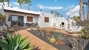 A white building with a patio, palm trees, and a garden with cacti and rocks. - Apartment Puerto Chico R with Sea View, Pool, Terrace & Wi-Fi (Playa Blanca)