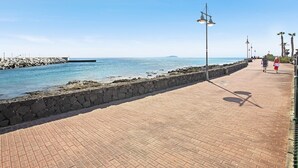 A paved walkway beside a body of water, with a stone wall and street lamps. - Apartment Puerto Chico R with Sea View, Pool, Terrace & Wi-Fi (Playa Blanca)