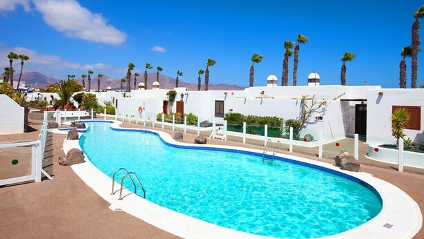 A swimming pool with a clear blue water, surrounded by white walls and palm trees. - Apartment Puerto Chico R with Sea View, Pool, Terrace & Wi-Fi (Playa Blanca)