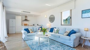 Una sala de estar moderna con un sofá azul claro, una mesa de centro redonda y una cocina al fondo.
