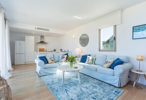 Un salon moderne avec un canapé bleu clair, une table basse ronde et une cuisine en arrière-plan.