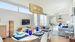 Una sala de estar moderna con comedor, televisor y un amplio ventanal.