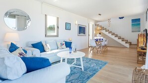 Una sala de estar moderna con un sofá blanco, una mesa redonda de centro y un comedor con sillas y una mesa.