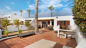 Une terrasse avec des meubles d’extérieur, des palmiers et un bâtiment blanc doté d’une cheminée en briques.