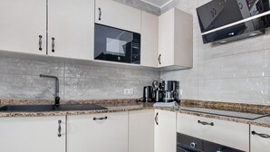 Une cuisine moderne avec des armoires blanches, un comptoir en granit, un four à micro-ondes encastré, une machine à café et un téléviseur fixé au-dessus du four.